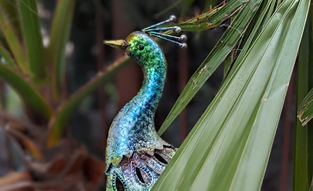 A metal painted peacock behind palm tree leaves.